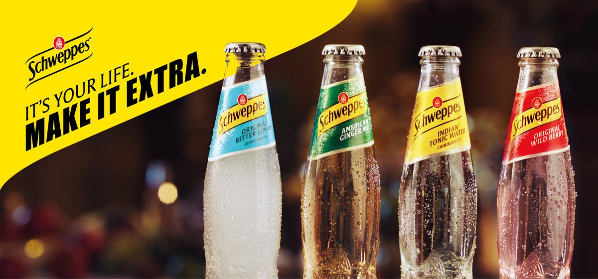 Vier Schweppes-Flaschen in unterschiedlichen Geschmacksrichtungen vor gelbem Hintergrund mit dem Schriftzug 'IT'S YOUR LIFE. MAKE IT EXTRA.'